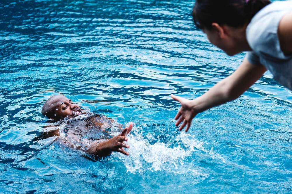 Person in pool reaching for help, outstretched hand offering assistance, water splash, safety concept.