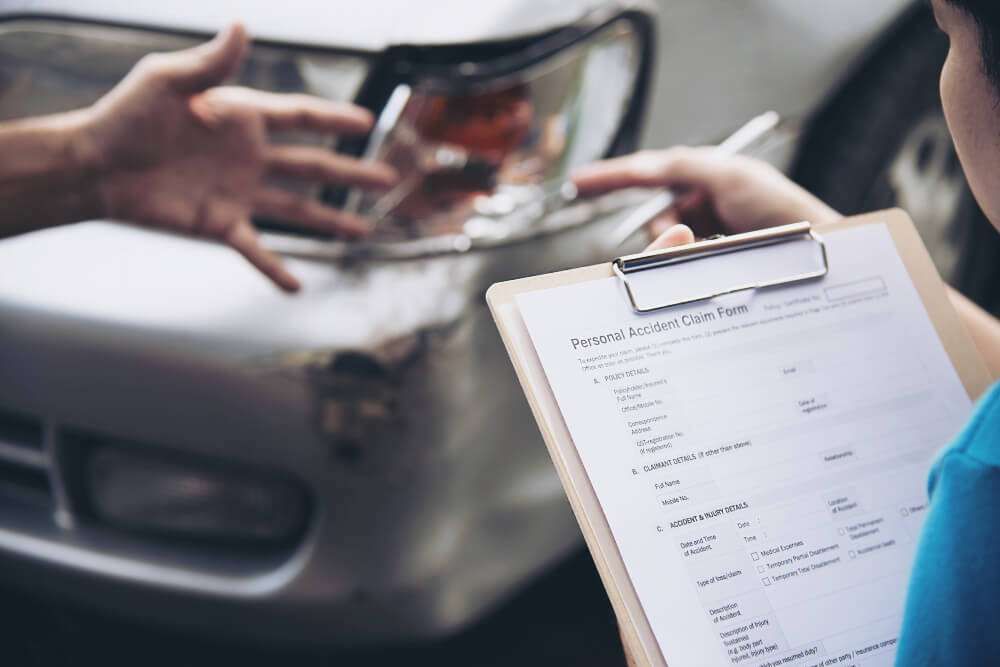 Person assessing car accident damage with a clipboard for personal accident claim form.