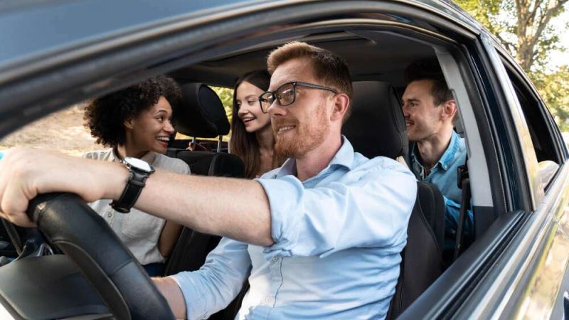 Smiling friends enjoy a road trip in a car during a sunny day drive.