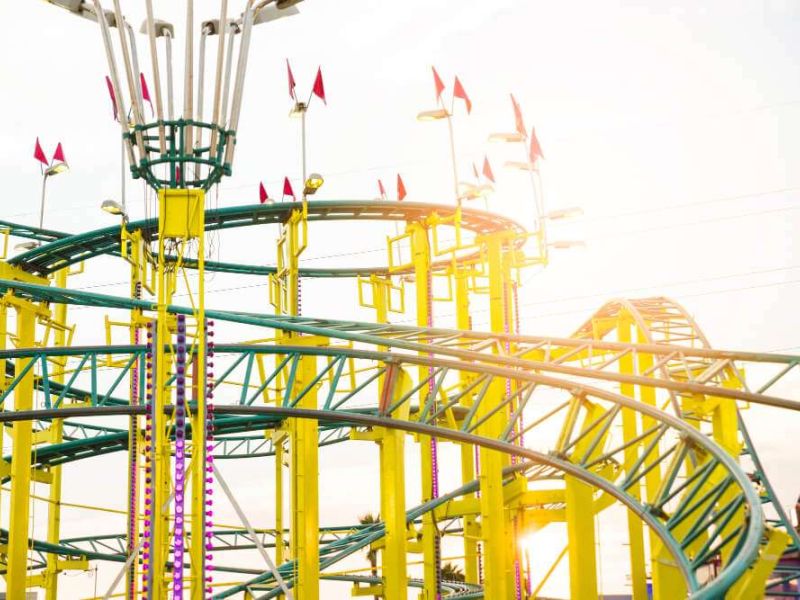 Colorful roller coaster with bright yellow tracks and red flags against a sunny sky at an amusement park.