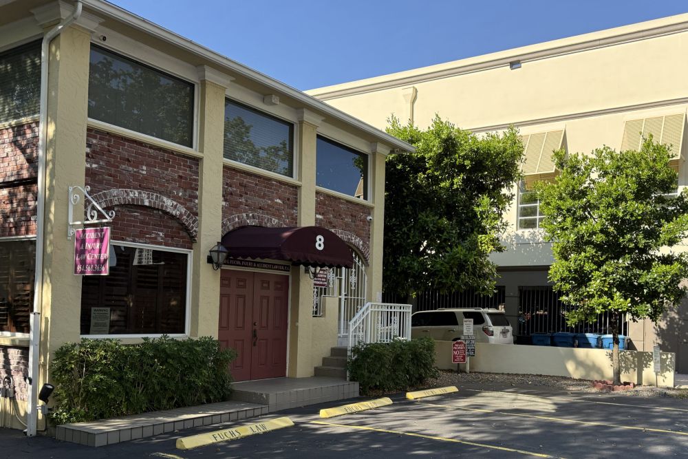 Two-story law office with a sign for accident and injury services, located in a sunny area with trees.