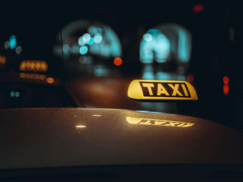 Yellow taxi sign glowing on parked cab at night with blurred city lights in the background.