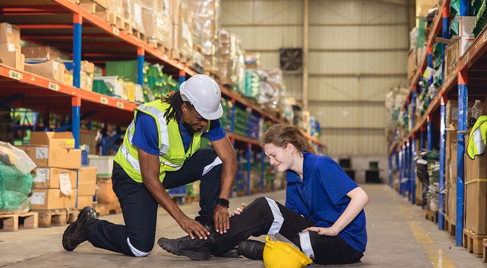 Worker assists injured colleague in warehouse, demonstrating safety protocols at workplace.