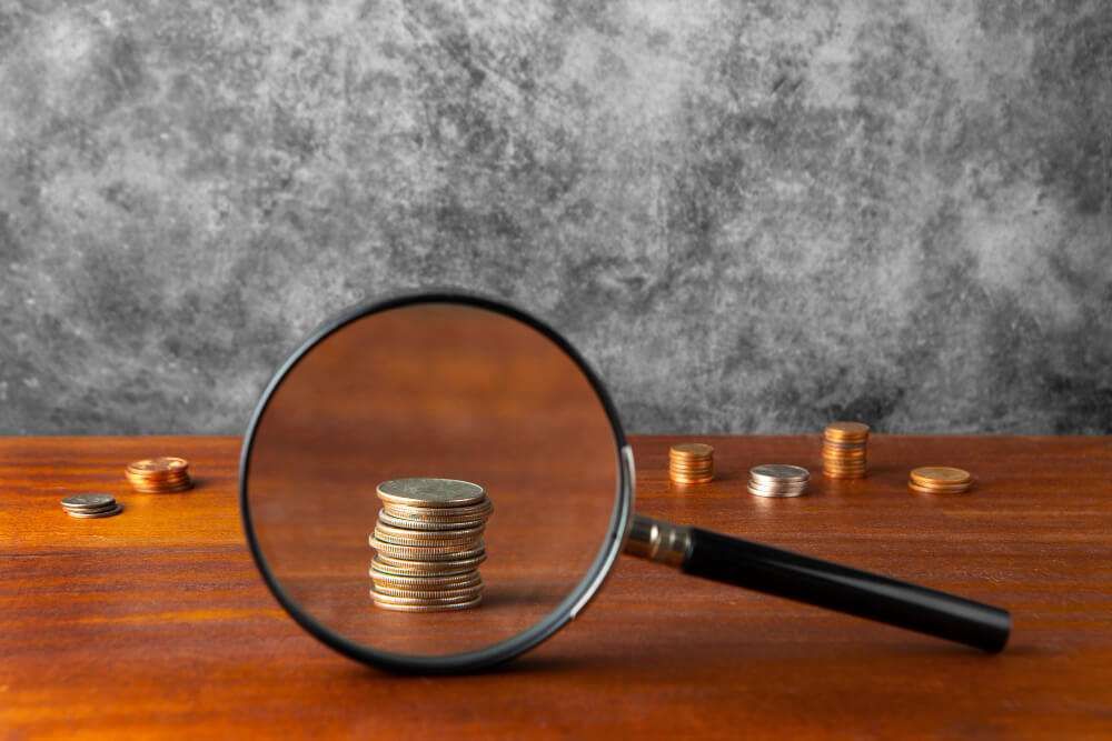Magnifying glass focusing on stacked coins on a wooden surface, emphasizing financial analysis and growth potential.