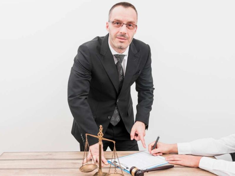 Male lawyer pointing to document with scales and gavel on desk, a client signing papers.