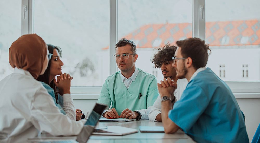 A multicultural medical team having a meeting around a table with laptops in a bright conference room.