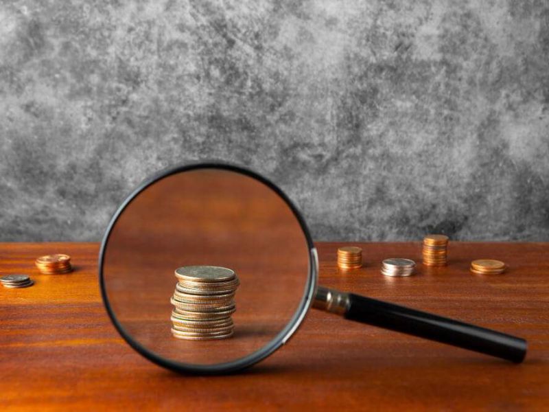 Magnifying glass focusing on stacked coins on a wooden surface, emphasizing financial analysis and growth potential.