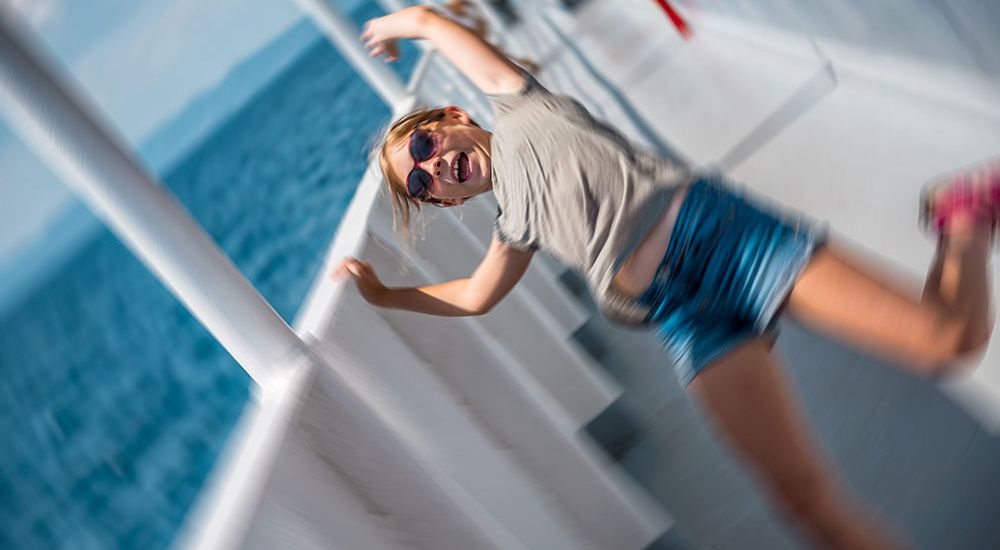 Person joyfully posing on a moving boat with a blurred ocean background.