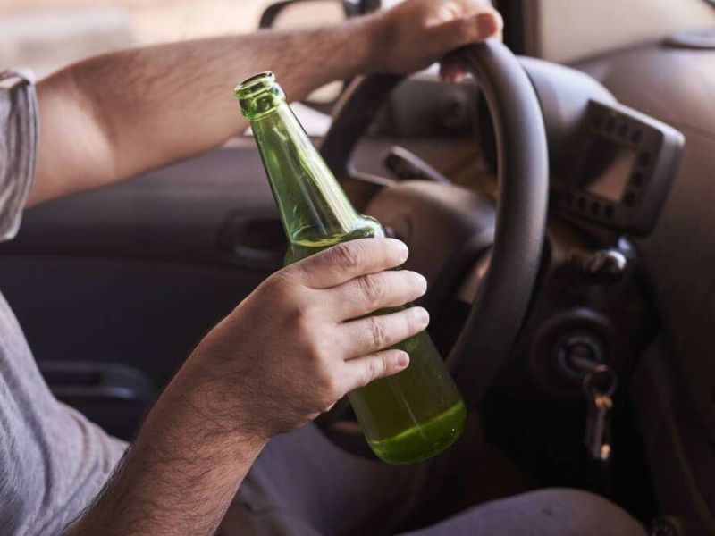 Driver holding a green bottle while steering a vehicle.