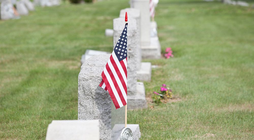 American flag on a gravestone in a cemetery, honoring veterans and Memorial Day remembrance.