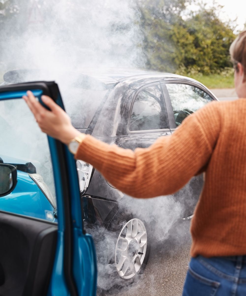 Person at car accident scene with smoking vehicles, appearing distressed.