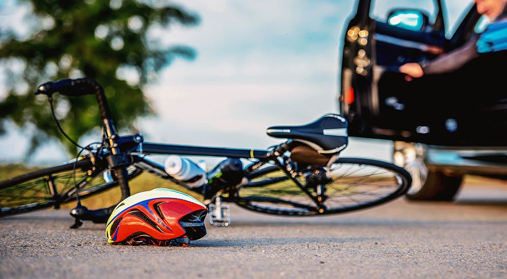 Bike accident scene with helmet on road and car door open, emphasizing road safety awareness and responsibilities.