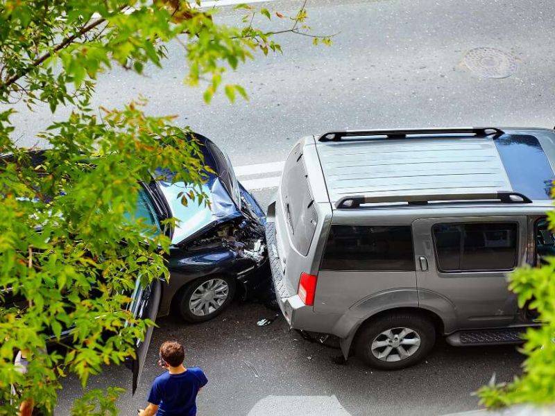 Two cars involved in a rear-end collision on a street, viewed from above through tree branches.