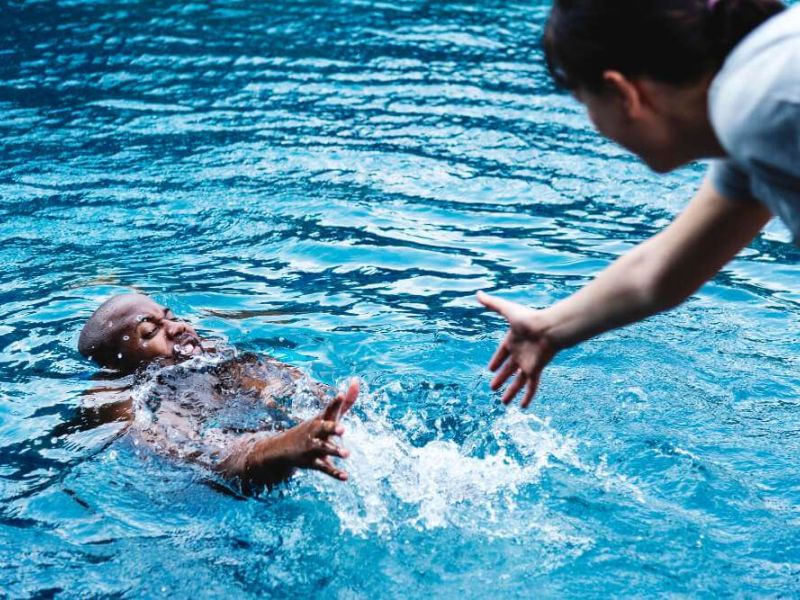 Person in pool reaching for help, outstretched hand offering assistance, water splash, safety concept.