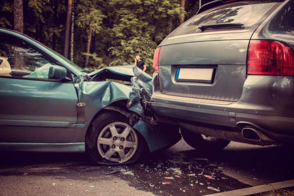 Two cars in a rear-end collision on a forest road, showing visible damage to vehicles' bumpers and hoods.