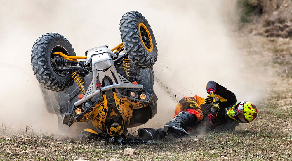 ATV rider falls during off-road race, flipping vehicle on dirt track, creating dust cloud.