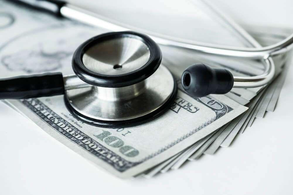 Stethoscope on stack of hundred-dollar bills symbolizing healthcare costs and financial planning.