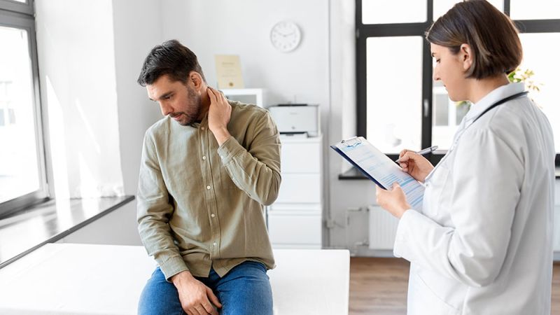 Male patient with neck pain consulting a doctor in a clinic.