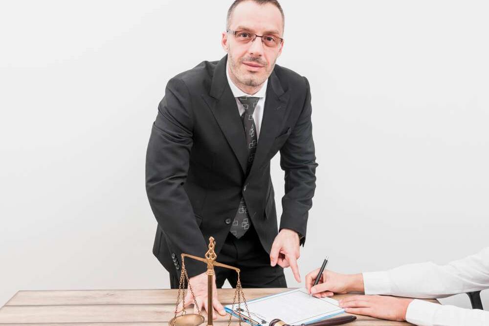 Male lawyer pointing to document with scales and gavel on desk, a client signing papers.