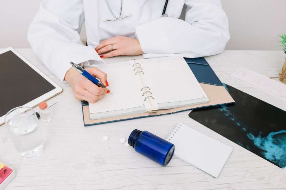 Doctor writing notes at desk with tablet, x-ray, and medication.