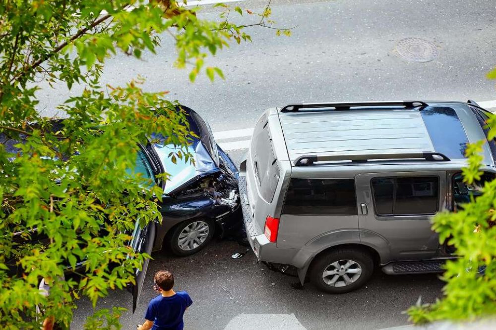 Two cars involved in a rear-end collision on a street, viewed from above through tree branches.