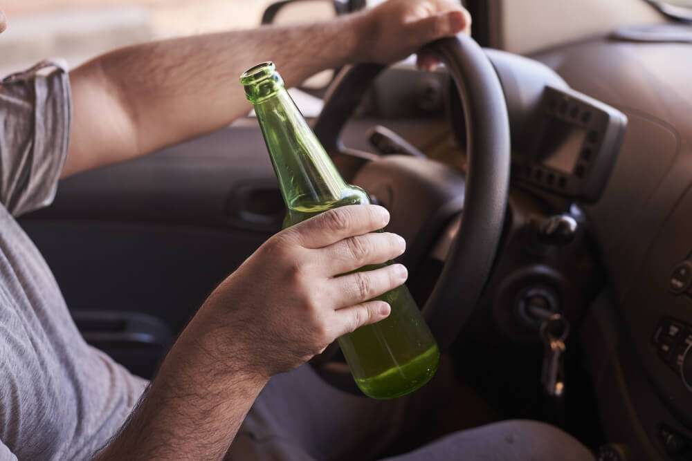 Driver holding a green bottle while steering a vehicle.