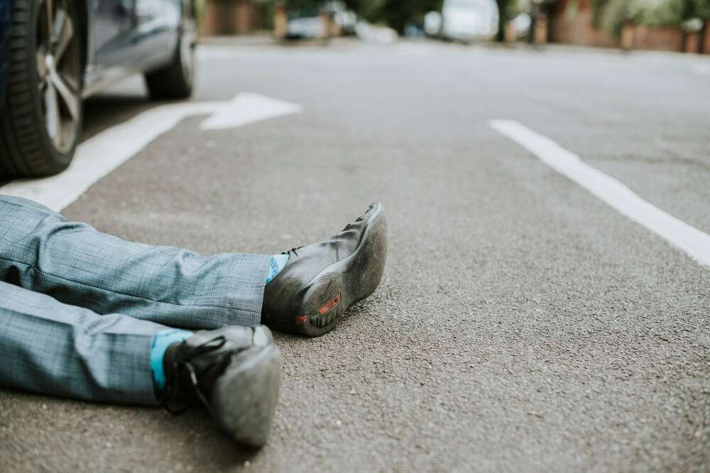 Man in suit lying on road beside car