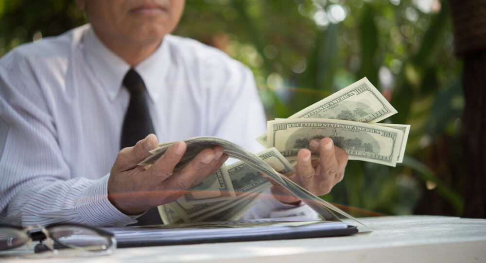Person counting dollar bills at outdoor desk