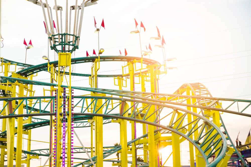 Colorful roller coaster with bright yellow tracks and red flags against a sunny sky at an amusement park.