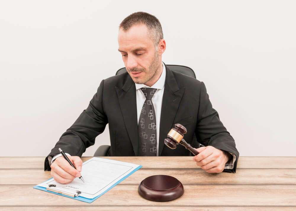 A judge in a suit signing a document while holding a gavel