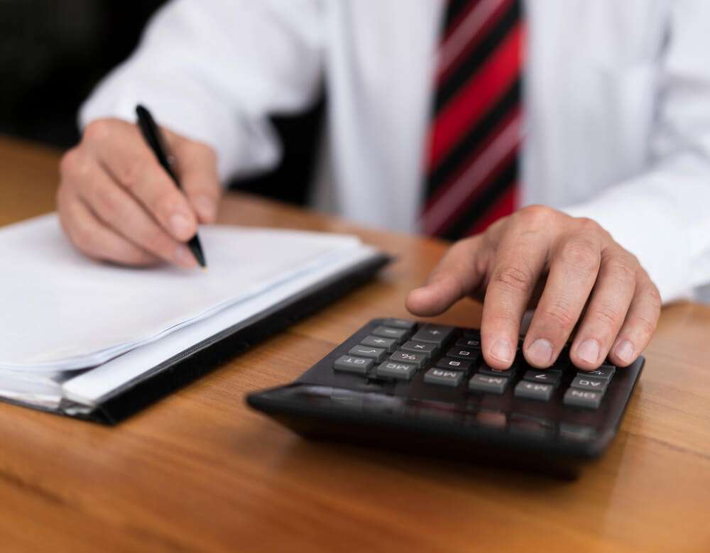 Person using a calculator and writing on paper at a wooden desk