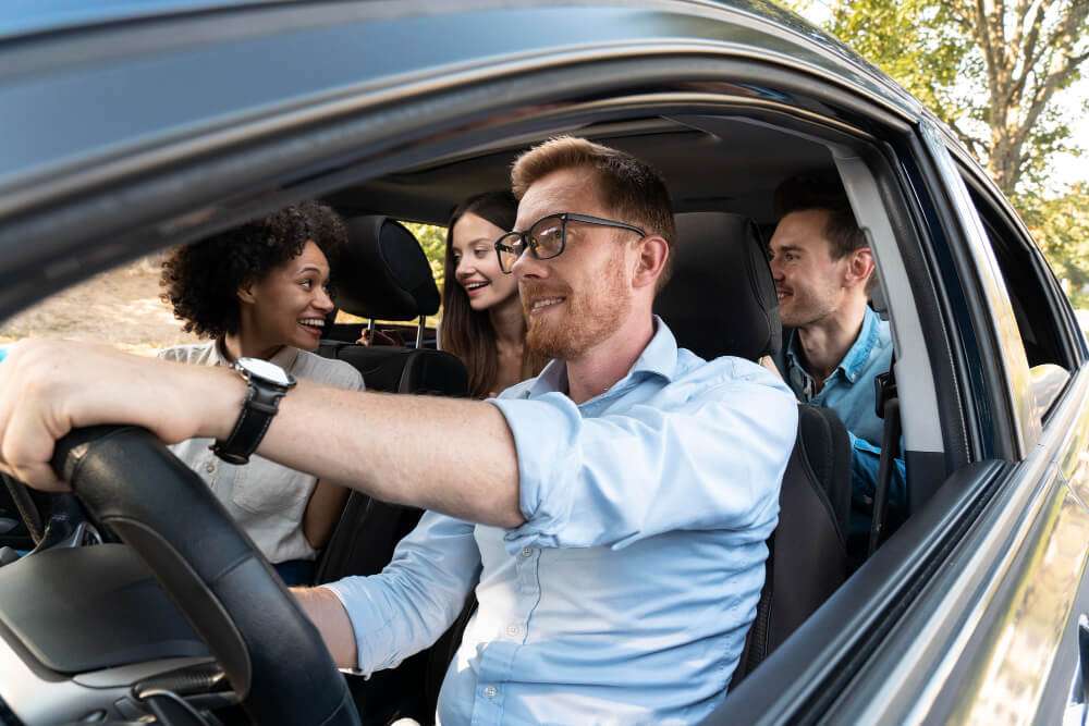 Smiling friends enjoy a road trip in a car during a sunny day drive.