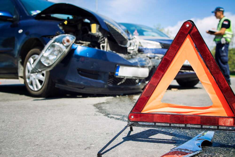 Car accident scene with warning triangle and police officer assessing damage on a bright day.