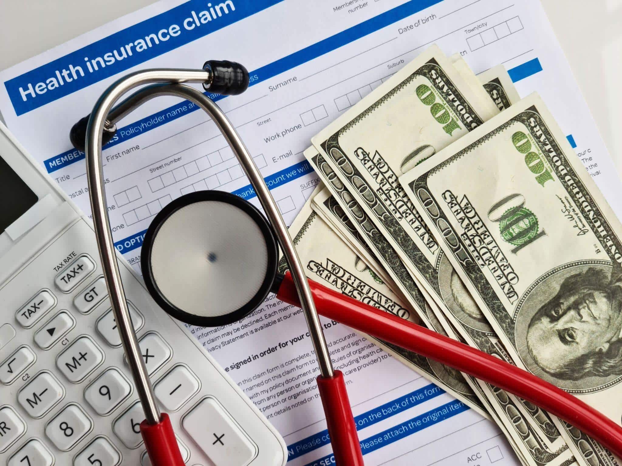 a calculator, stethoscope, and money on top of a table, there is a form titled "health insurance claim"