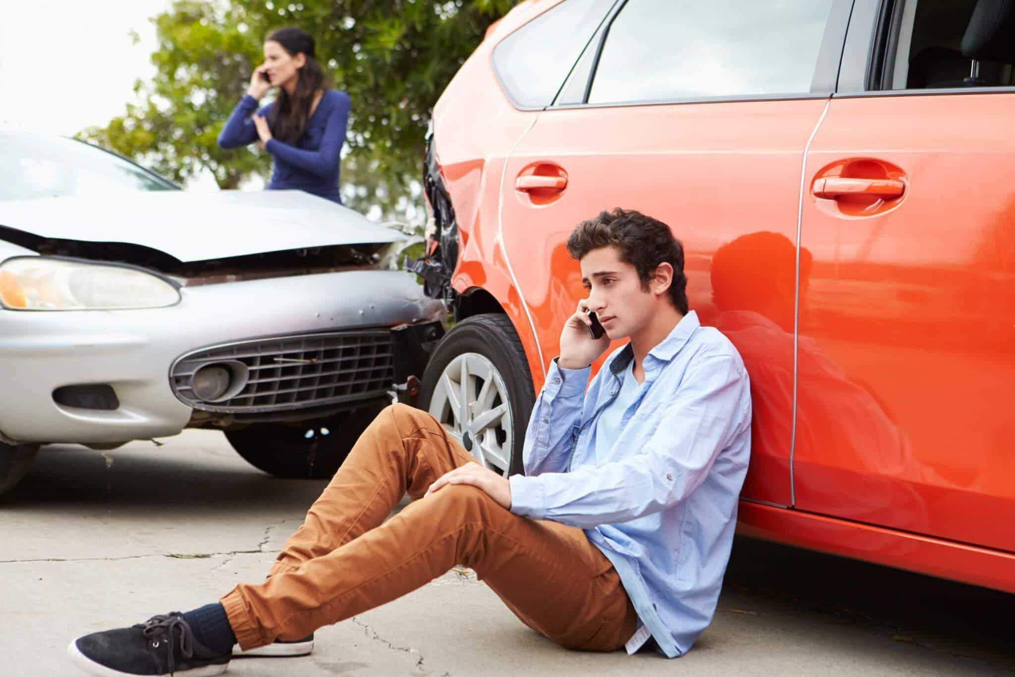 a man sitting on the ground next to a car talking on a cell phone